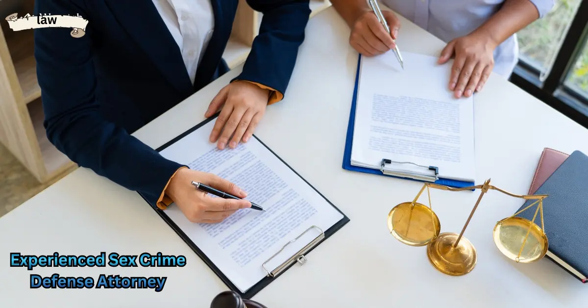Two professionals sit at a desk reviewing and signing legal documents, with a golden justice scale and folders placed nearby.